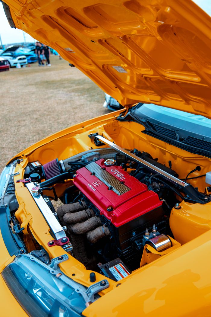 Vivid yellow car with red engine on display at outdoor event.